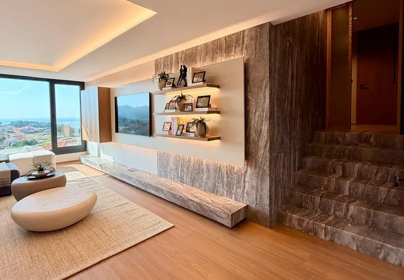Salón terminado con pared revestida en efecto piedra, estantes iluminados y vistas al mar