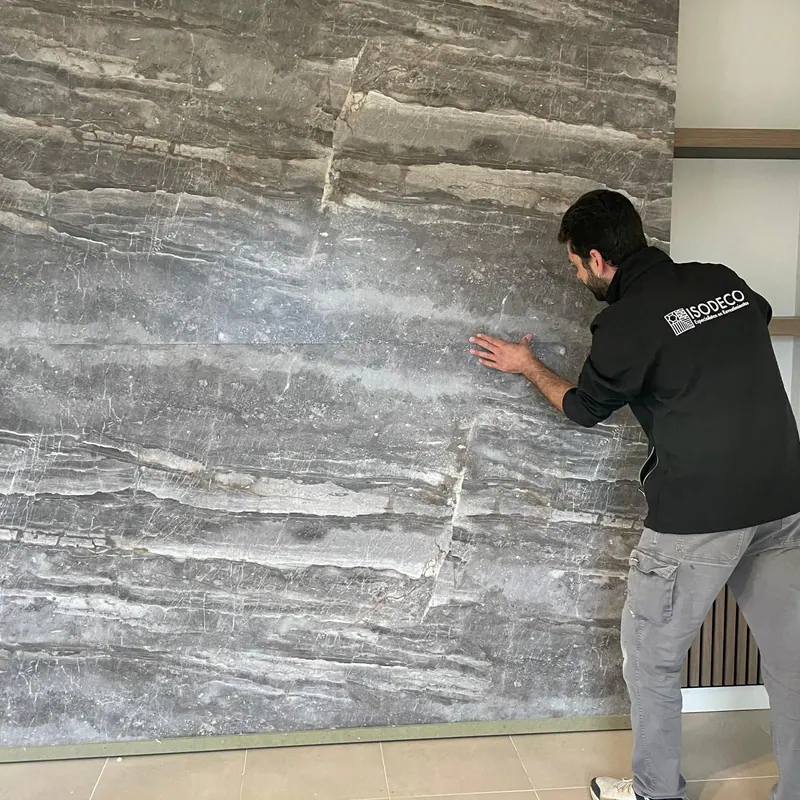 Un operario coloca a mano un panel grande de efecto piedra sobre una pared